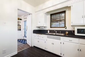 A kitchen with white cabinets, a black countertop, a window, and a microwave. - Clover Cottage - 1 mile to ND - Cozy Getaway (South Bend)
