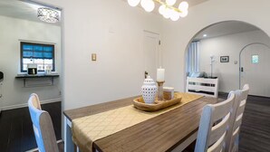 Una zona de menjador amb taula de fusta, cadires, un lampadari i un mirall.