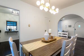 A dining area with a wooden table, chairs, a chandelier, and a mirror. - Clover Cottage - 1 mile to ND - Cozy Getaway (South Bend)