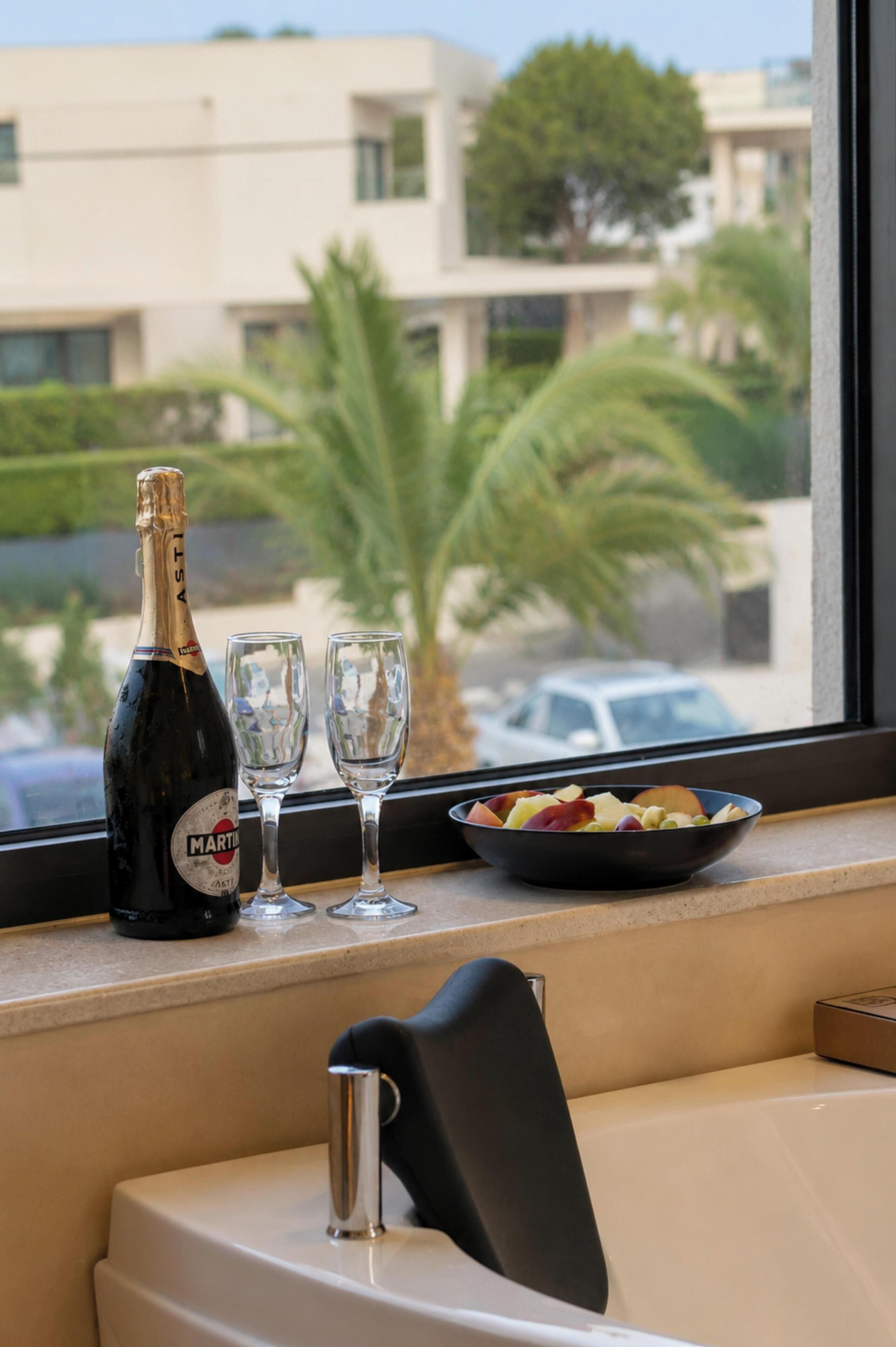 Eine Champagnerflasche, zwei Gläser und eine Schale mit Obst auf einem Fensterbrett.