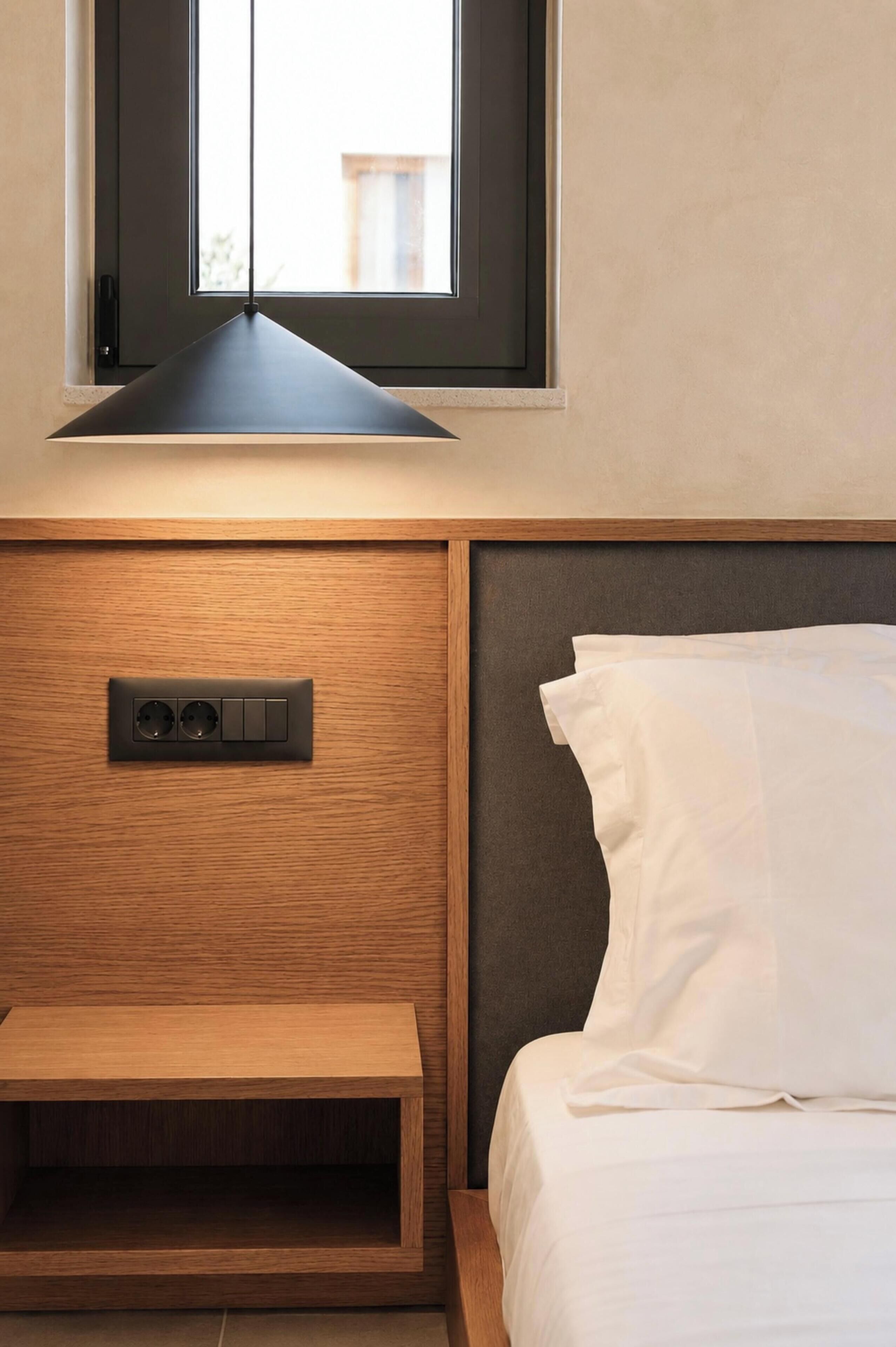 Ein Schlafzimmer mit einem Bett, einem Nachttisch mit Steckdose, einem Fenster und einer eingebauten Ablagefläche.