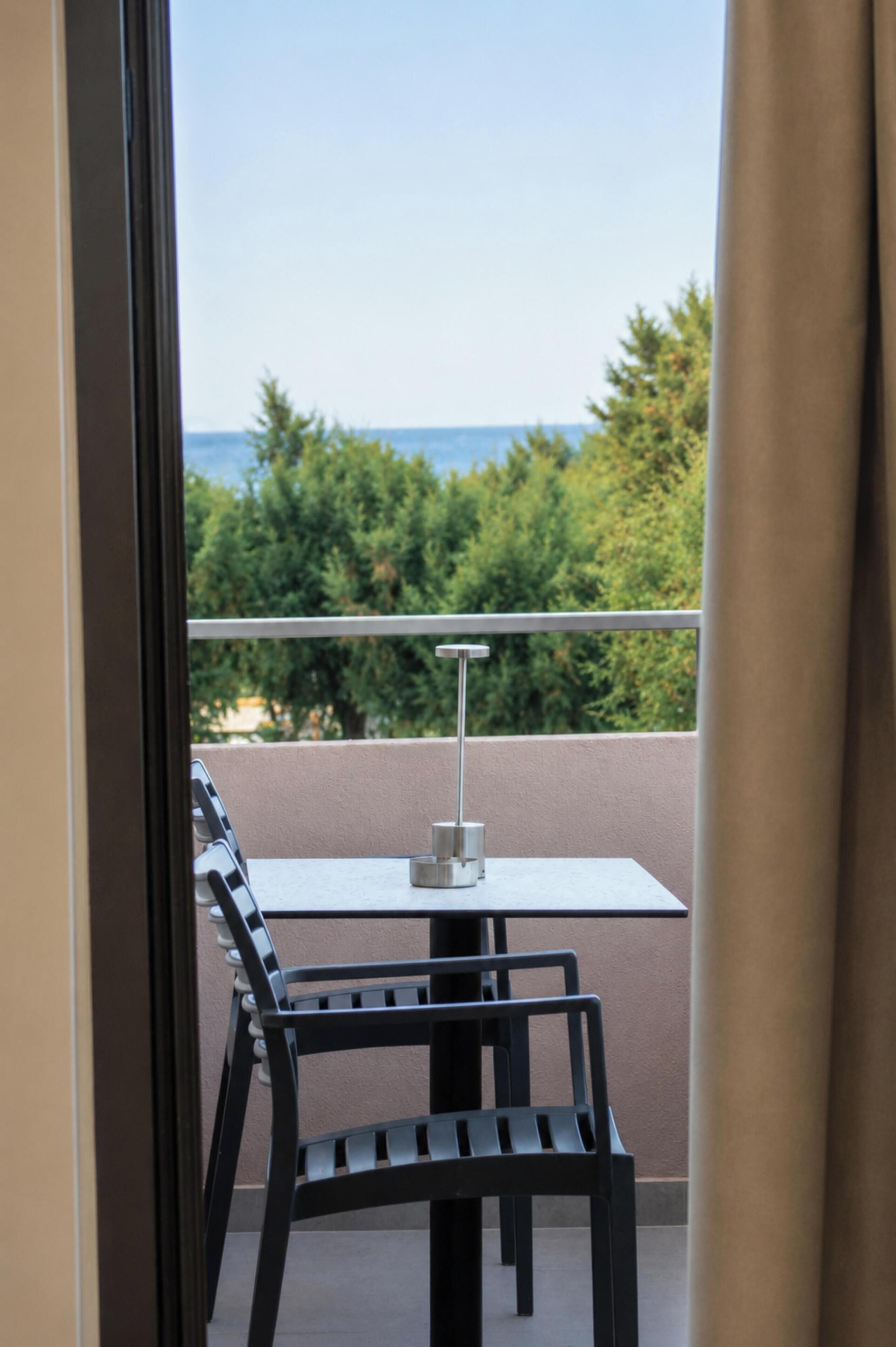 Un balcón con una mesa y sillas, con vistas a árboles y al mar.
