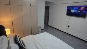 A hotel room with a bed, a TV mounted on the wall, and a hallway leading to another room. - Luxury Two bedroom Apartment  in  kileleshwa (Nairobi)