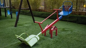 Ein Spielplatz mit Wippe, Schaukel und Rutsche.