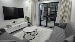 A modern living room with a flat-screen TV, a sofa, a coffee table, and a sliding glass door leading to a dining area. - Luxury Two bedroom Apartment  in  kileleshwa (Nairobi)