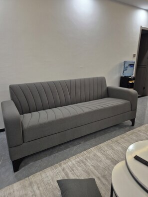 Ein graues Sofa in einem Raum mit Wasserspender und einem kleinen Tisch.