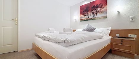 Habitación de hotel con cama, mesita de noche, lámpara de pared y un cuadro.