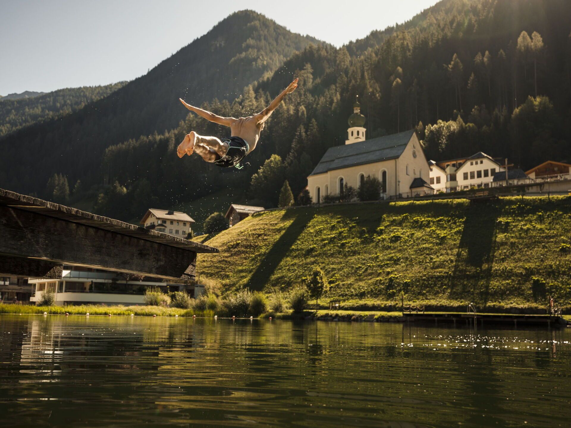 A person performing a backflip over a body of water with a mountainous landscape in the background.