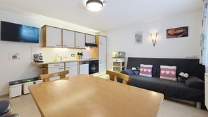 Um espaço compacto com mesa de jantar, cozinha compacta, sofá e televisão de tela plana na parede.