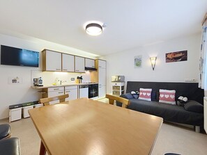 Ein kleiner Wohnbereich mit Esstisch, Küchenzeile, Sofa und einem an der Wand befestigten Flachbildfernseher.