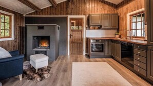 A rustic kitchen with wooden walls, a fireplace, modern appliances, and a cozy seating area. - Cozy mountain cabin at 962m (Ål)