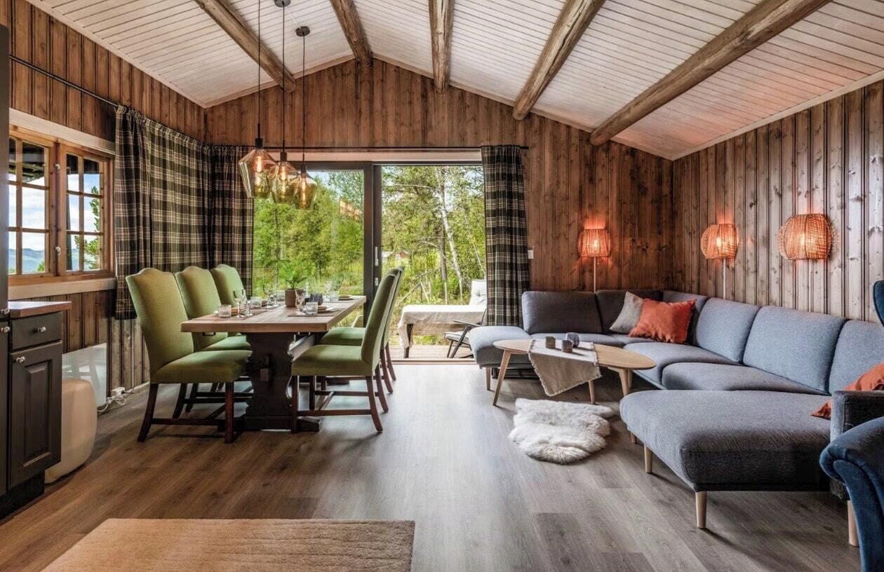 Un intérieur de chalet chaleureux avec un coin repas, un canapé et de grandes fenêtres donnant sur le paysage extérieur.