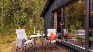A wooden deck with two chairs and a table, a glass door leading to an interior space, and a forested backdrop. - Cozy mountain cabin at 962m (Ål)