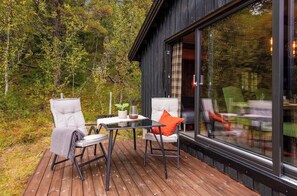A wooden deck with two chairs and a table, a glass door leading to an interior space, and a forested backdrop. - Cozy mountain cabin at 962m (Ål)