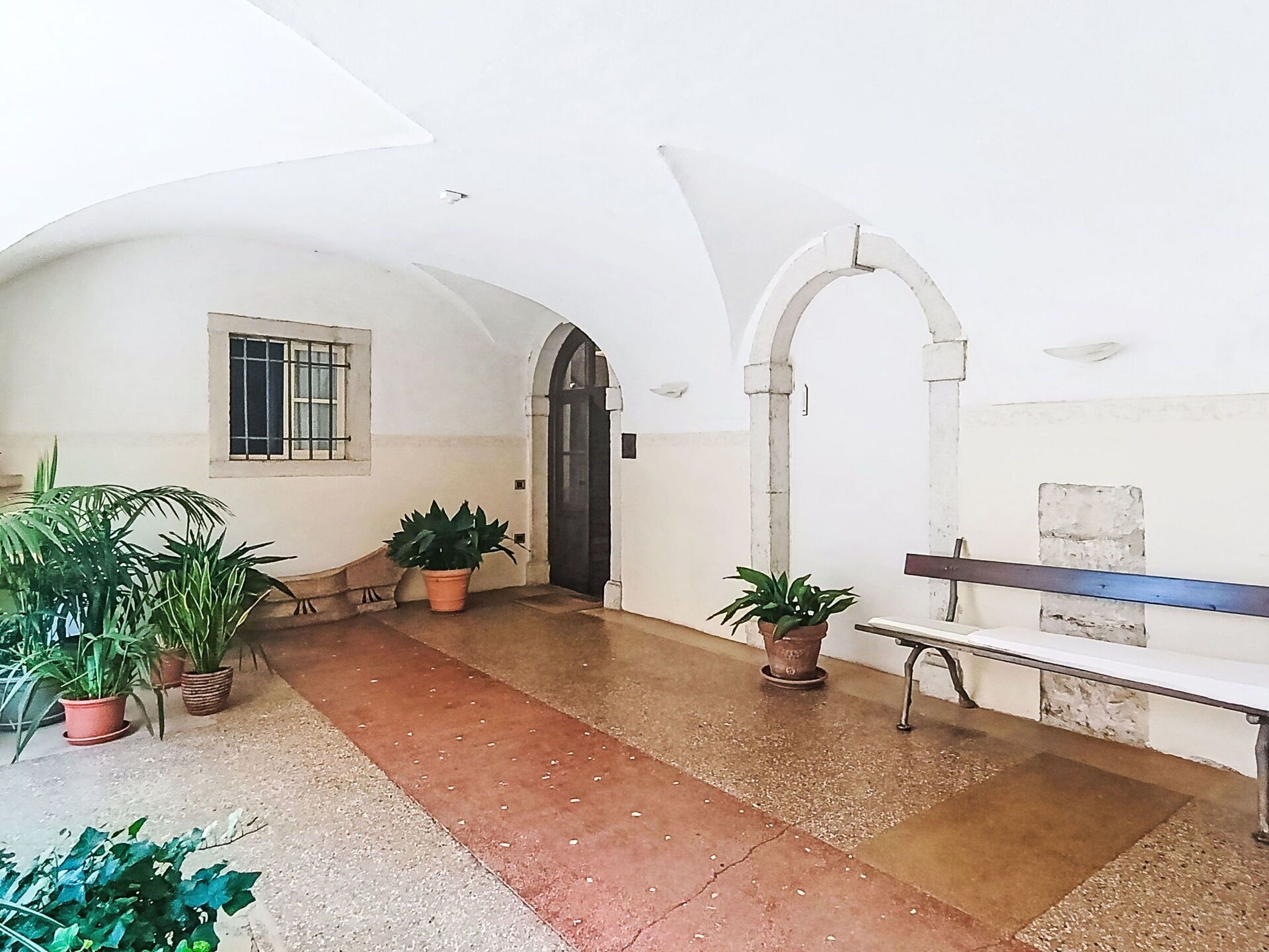 A corridor with arches, a bench, and potted plants.