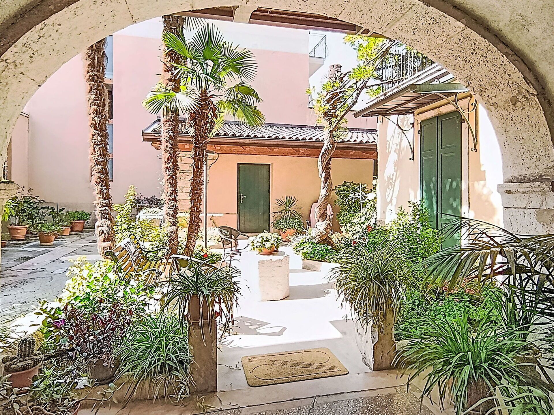 Une cour extérieure agrémentée d’une arche en pierre, de plantes en pot et d’un bâtiment doté d’un toit en tuiles.