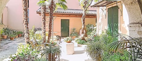 An outdoor courtyard with a stone archway, potted plants, and a building with a tiled roof.