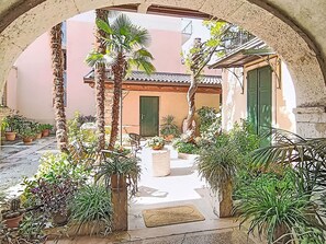 Um pátio exterior com arco de pedra, plantas em vasos e um edifício com telhado de azulejos.