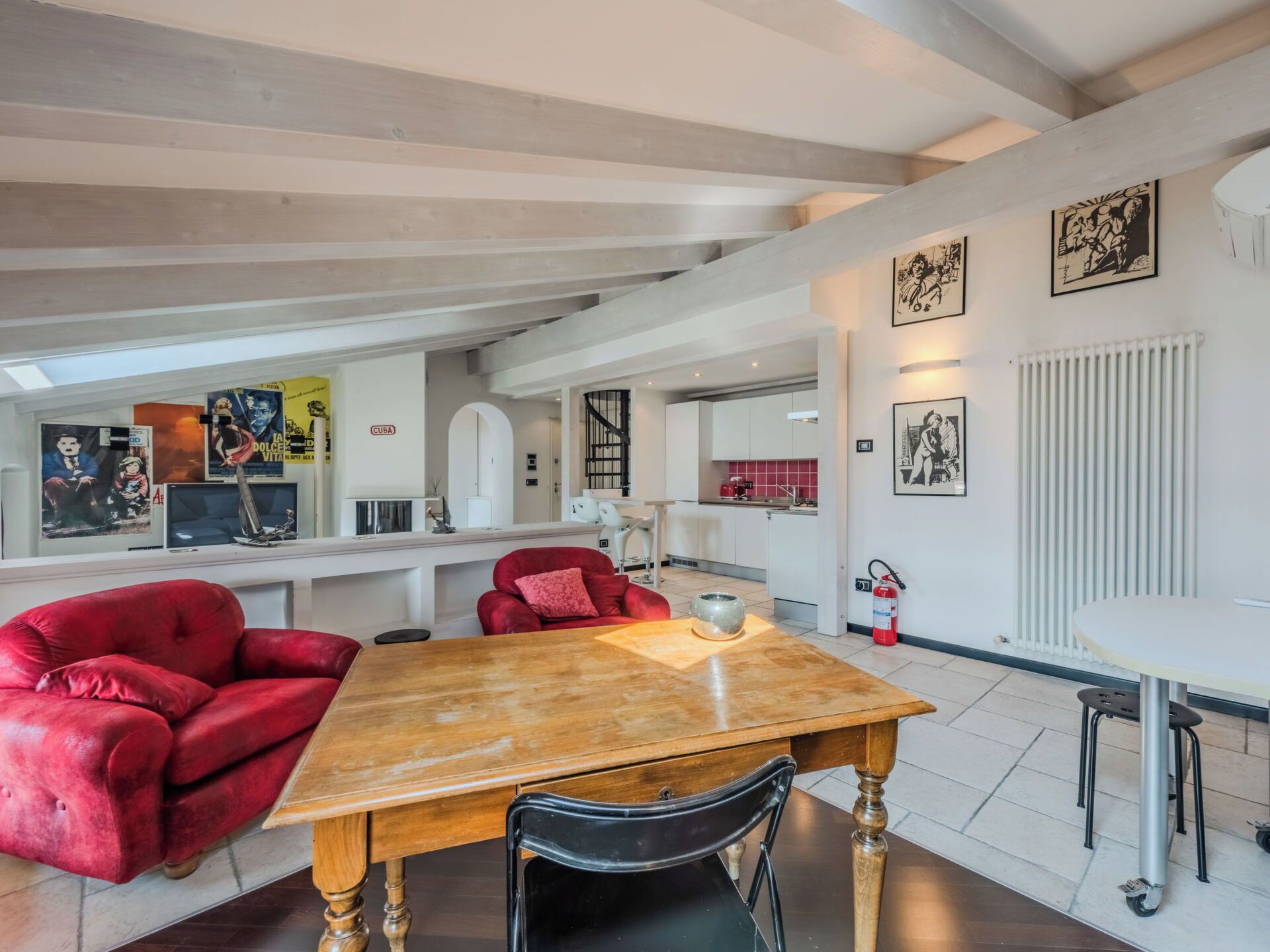 A spacious living area with a wooden table, red sofas, and a kitchen in the background.