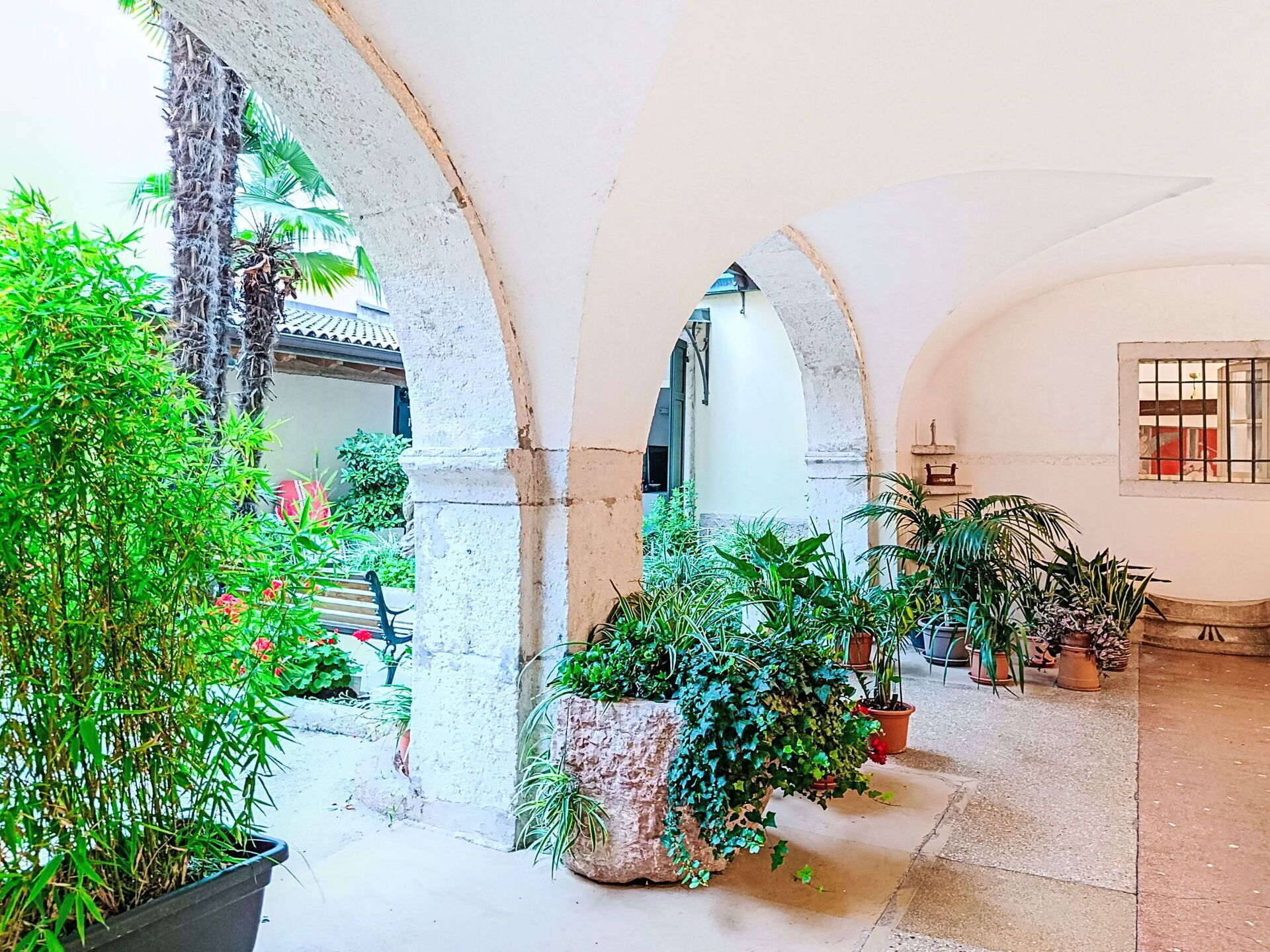 Ein Innenhof mit Bögen, Topfpflanzen und einer Bank.
