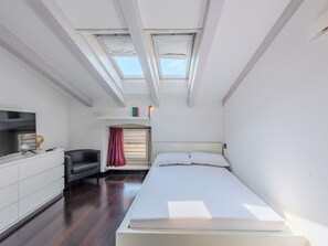 Quarto com cama, televisão, escrivaninha e cadeira. Há claraboias acima da cama.
