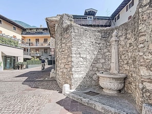 Una strada acciottolata con un muro di pietra, un uomo in bicicletta e edifici con balconi.