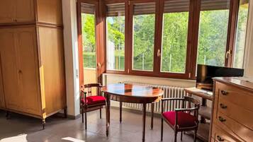 Une pièce avec une grande fenêtre, un meuble en bois, une table ronde et deux chaises.