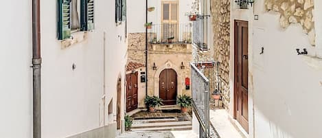 A narrow alleyway with stone steps leading to a building with a wooden door and a balcony with potted plants.