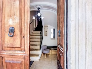 Eine Holztür mit Metallbeschlag, eine Treppe zu einem Raum mit einem grauen Sessel und einer Deckenleuchte.