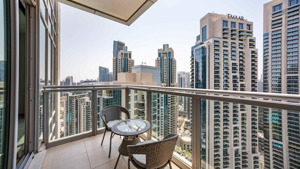 A balcony with a glass table and wicker chairs, overlooking a cityscape with high-rise buildings. - Cozy 1BR Steps From Burj Khalifa Mall (Dubai)