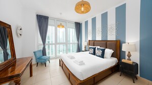 A hotel room with a large bed, a desk, a chair, a nightstand, a lamp, and a view of the city through the window. - Cozy 1BR Steps From Burj Khalifa Mall (Dubai)