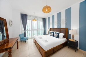 A hotel room with a large bed, a desk, a chair, a nightstand, a lamp, and a view of the city through the window. - Cozy 1BR Steps From Burj Khalifa Mall (Dubai)