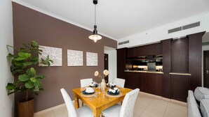 A dining area with a wooden table set for two, flanked by white chairs, a potted plant, and wall-mounted artwork. - Cozy 1BR Steps From Burj Khalifa Mall (Dubai)