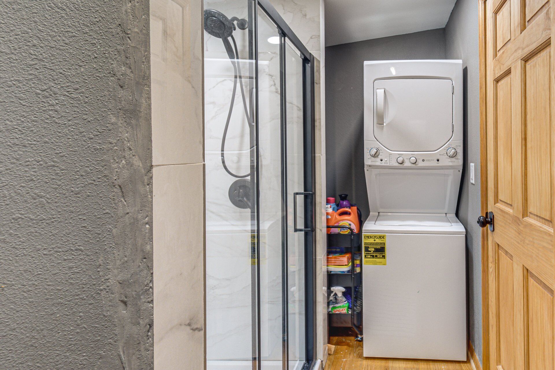 Une salle de bain compacte dotée d’une cabine de douche en verre, d’un lave-linge et d’un sèche-linge intégrés, et d’une porte en bois.