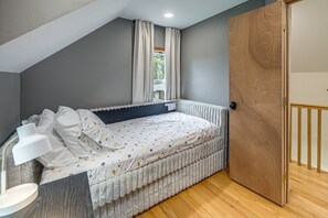 A bedroom with a bed, a nightstand, a window with curtains, and a wooden door.
