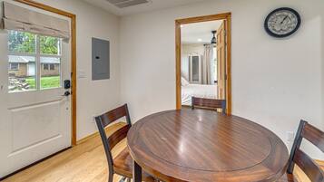 Un comedor con una mesa redonda de madera y cuatro sillas, un reloj en la pared y una puerta que da a otra habitación.
