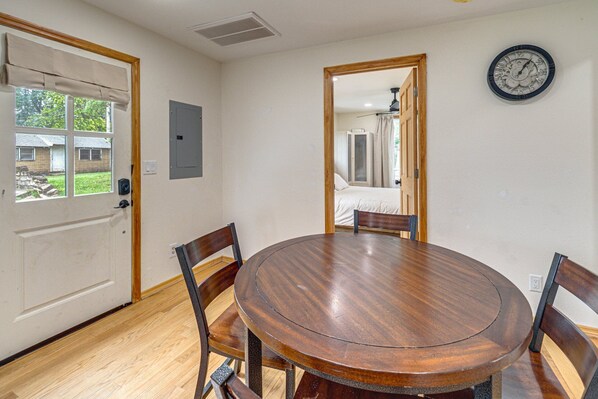A dining area with a round wooden table and four chairs, a clock on the wall, and a door leading to another room.