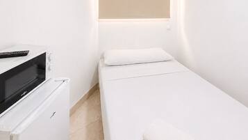 Una habitación pequeña y moderna con una cama, un escritorio con una computadora y una lámpara de pared.
