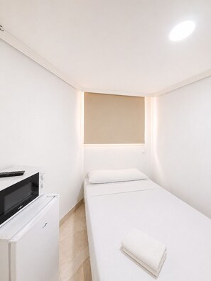 A small, modern room with a bed, a desk with a computer, and a wall-mounted light. - Hostel La Campana (Madrid)