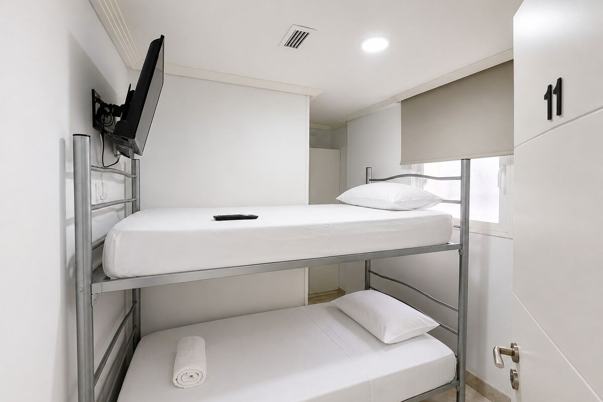 Una cama litera con un televisor montado encima, una ventana con vistas y una puerta con un número.