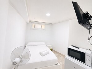A hotel room with a bed, a TV, a fan, and a window.