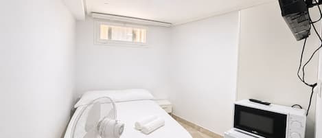 A bedroom with a bed, a standing fan, a microwave, and a small heater.