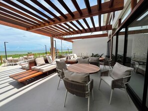 Um pátio externo com pérgola de madeira, áreas de estar e vista para o mar.