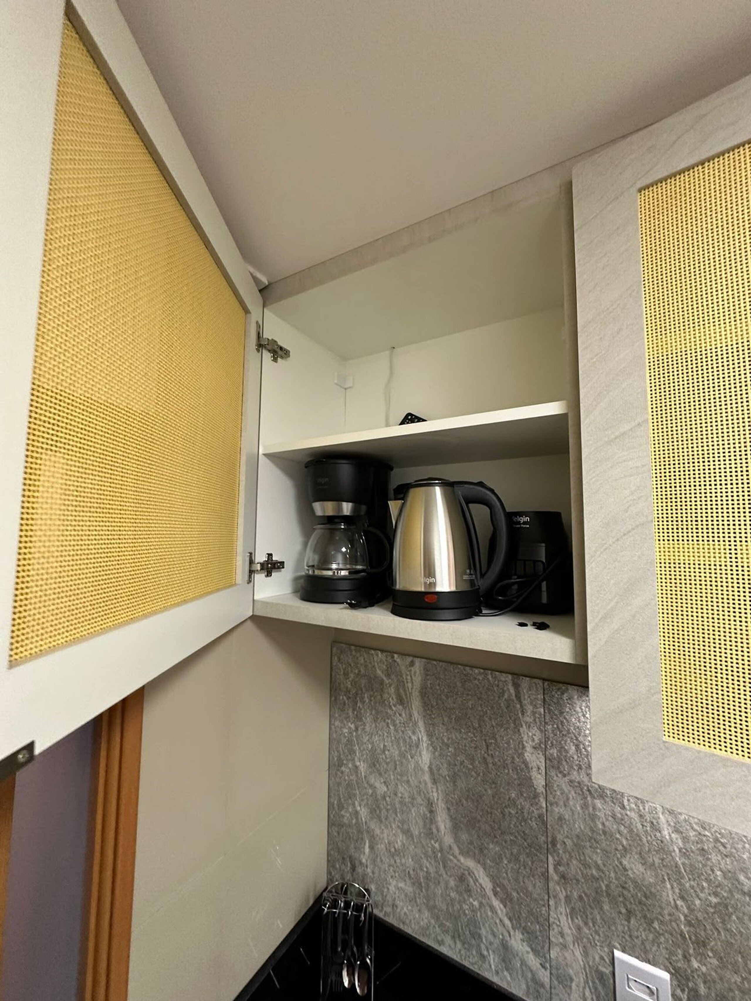 Uma cozinha com cafeteira, chaleira e micro-ondas na bancada.