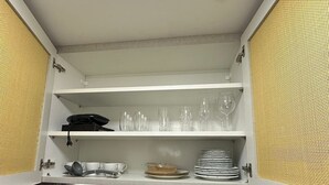 Ett kompakt kök med en inbyggd hylla ovanför diskhon, en kaffemaskin och en liten träpall.