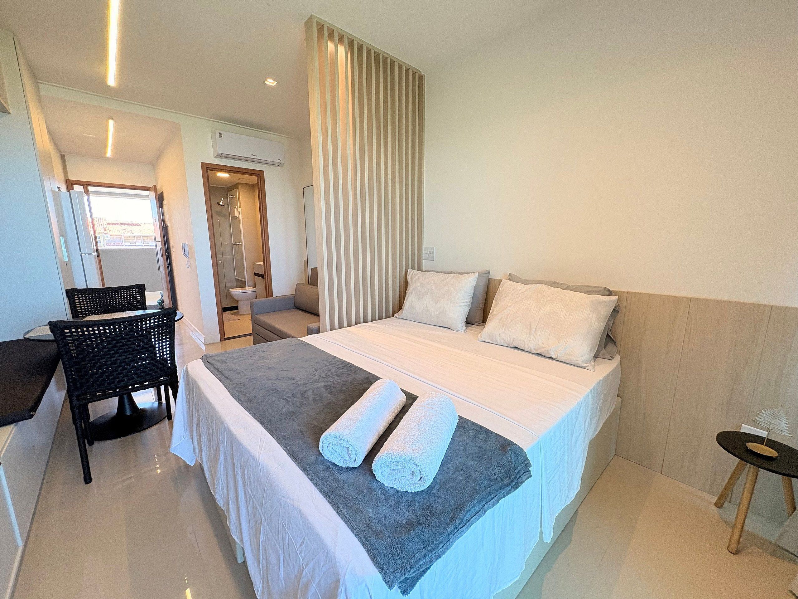 A hotel room with a bed, a chair, a small table, and a bathroom visible through an open door.
