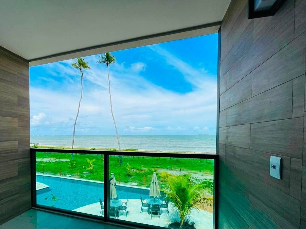 Quarto com uma grande janela que dá para uma piscina e uma praia, paredes de madeira e vista para o oceano.