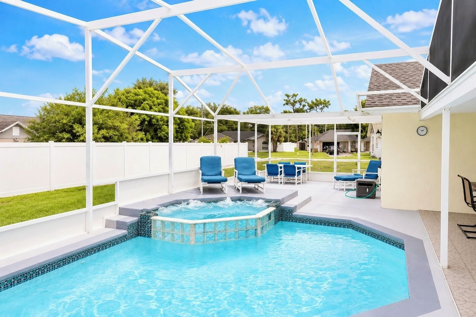 A backyard swimming pool with a hot tub, surrounded by a covered patio with blue chairs and a table.
