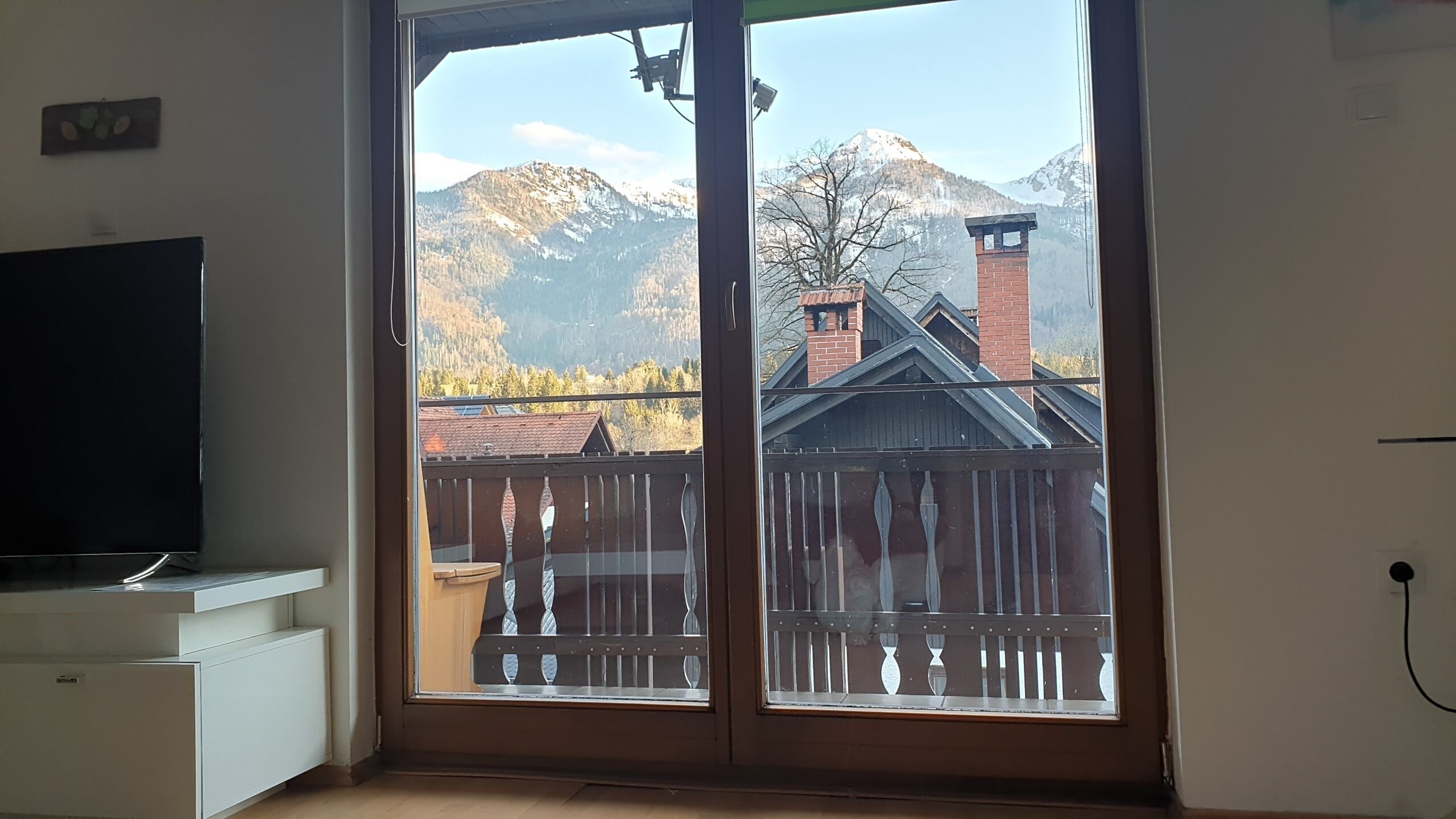 Una habitación con puerta corrediza de vidrio que da a un balcón con vistas a montañas y una valla de madera.