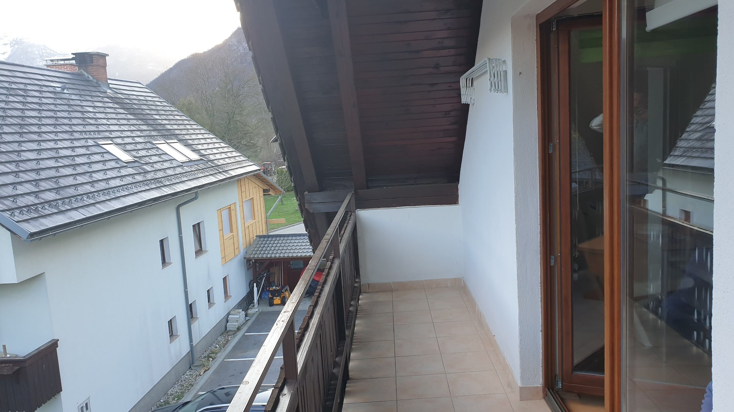 A balcony with a view of a mountain, a wooden door, and a window with a view of a building with a tiled roof.